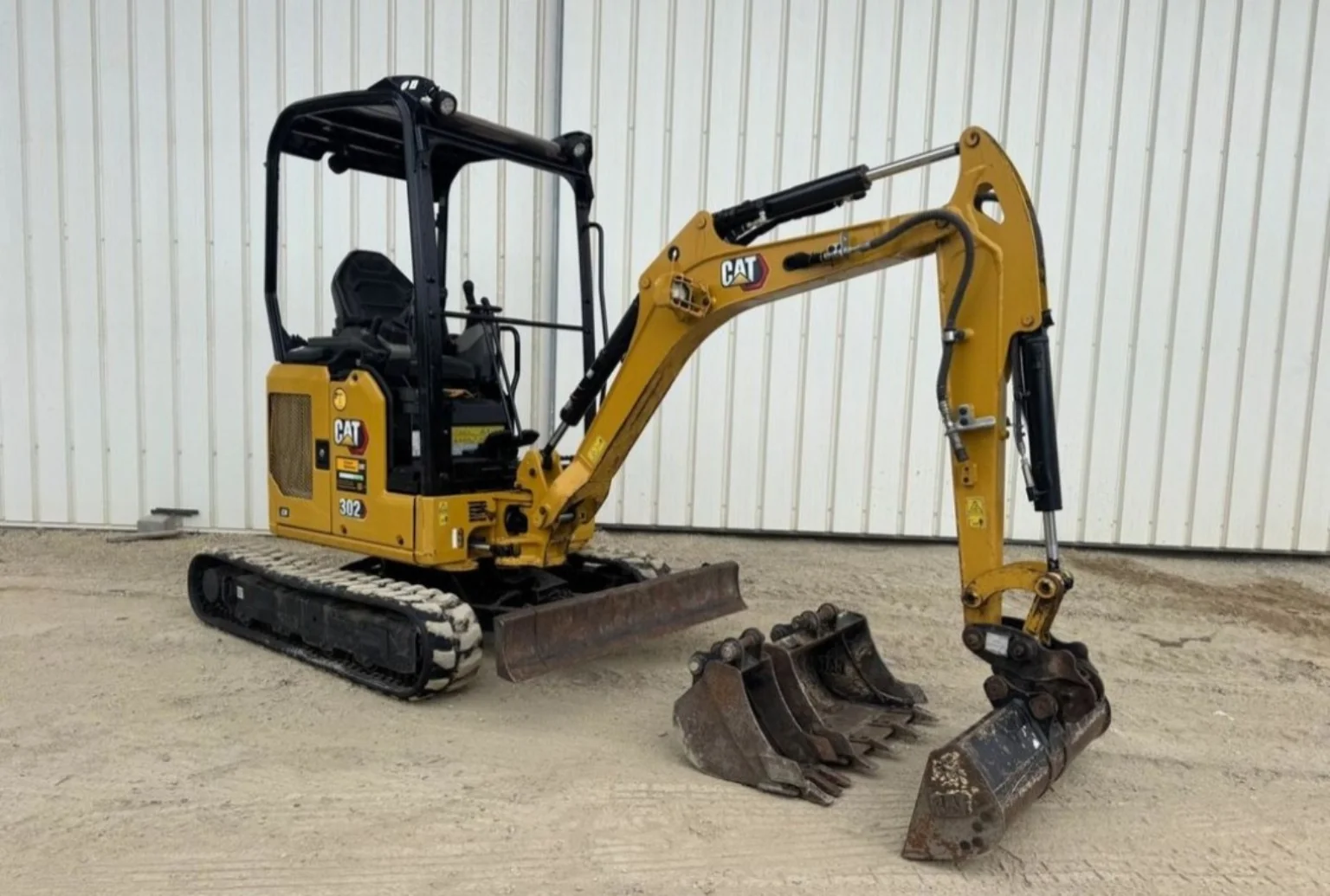 Mini-pelle Caterpillar CAT 302 jaune avec plusieurs godets.