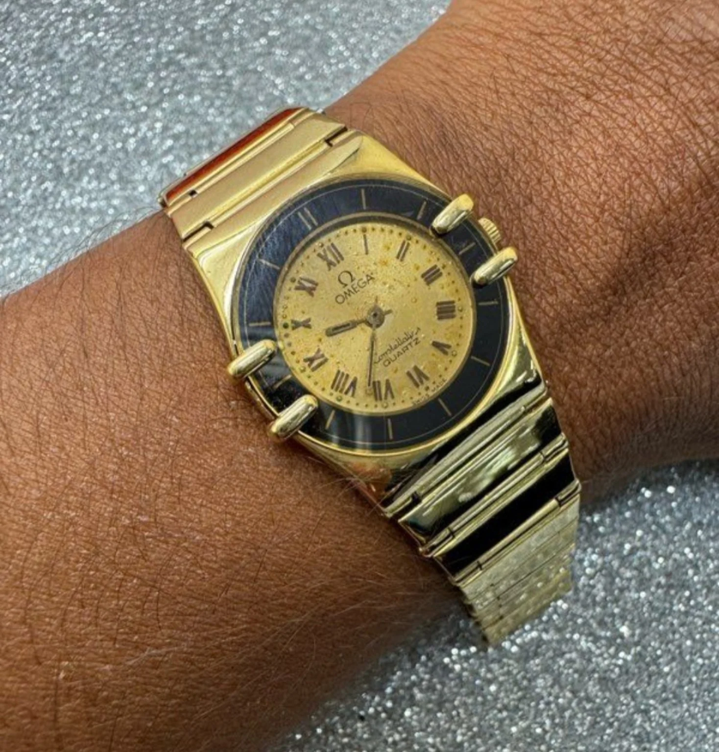 Montre dorée avec cadran à chiffres romains, portée au poignet.